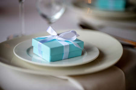 Festive table setting with handmade gift box on plate. Light blue handmade gift box in plate on wedding table.の写真素材