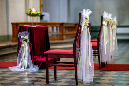 Beautiful floral wedding decoration in a church. Christian church decoration for wedding marriage ceremony. Wedding decor for chairs from flowers, veils and ribbons in church.の写真素材