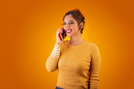 Woman on yellow background using cell phone and smiling