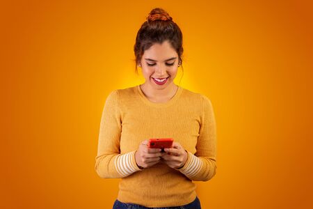 Woman on yellow background using cell phone and smilingの写真素材