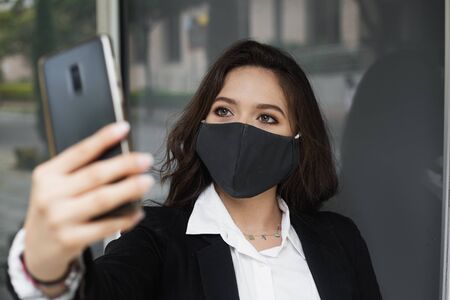 female businesswoman taking a selfie leaving her office wearing a maskの写真素材