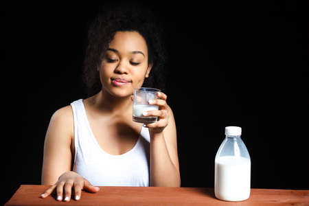 African cheerful girl with a glass of milk on a dark background, the contrastの写真素材