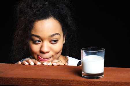 African cheerful girl with a glass of milk on a dark background, the contrastの写真素材