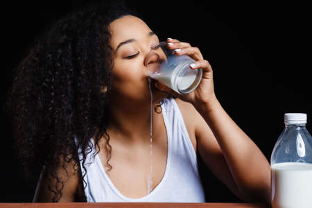 African cheerful girl with a glass of milk on a dark background, the contrastの写真素材