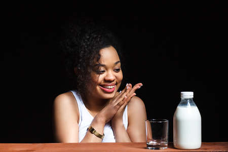 African cheerful girl with a glass of milk on a dark background, the contrastの写真素材