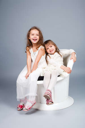 Two little funny and laughing girl in white clothes stand and hold hands.の写真素材