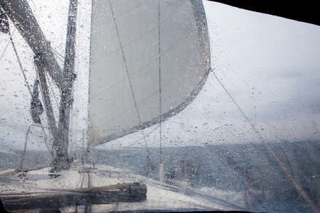 view through the glass with raindrops on the sea with sailing yachtの写真素材