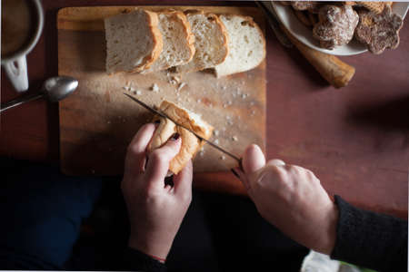 Woman cuts bread on an old wooden table. selective focus. natural light from windowの写真素材