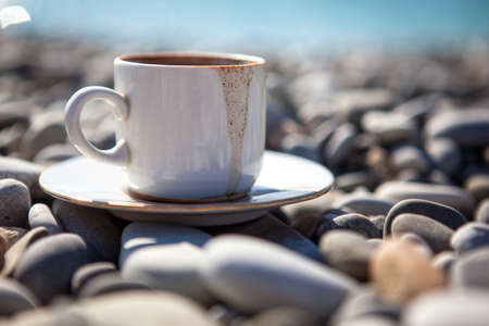 A cup of spilled coffee stands on stones near the sea shore, close up.の写真素材