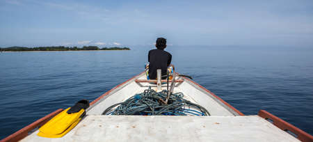 A man sits on the front of a fishing boat looking at a beautiful evening oceanの写真素材