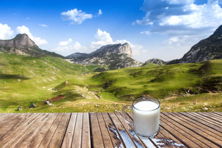 Mug of milk on a wooden table in the mountains. View of the small farm. Sun light and refreshing in the morning.の写真素材
