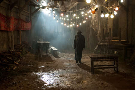Silhouette of a man in a coat and hat in a dark alley on a rainy nightの写真素材