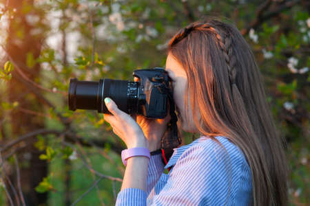 Beautiful young girl taking pictures in the forest. The girl with the camera. Tourist. Sunset. Summer eveningの写真素材