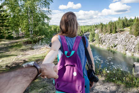 Tourist woman with backpack holding man by hand and walking down the mountain valleyの写真素材