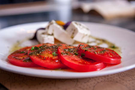 Mozzarella with tomatoes, italian herbs and rucola on a white plate on a wooden table, closeupの写真素材