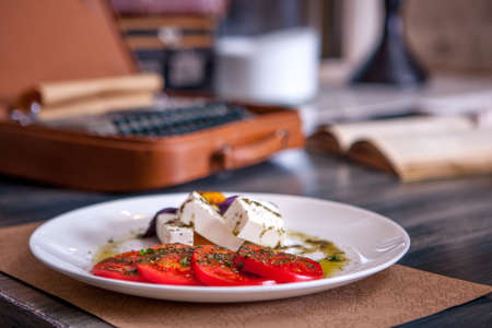 Mozzarella with tomatoes, italian herbs and rucola on a white plate on a wooden table, closeupの写真素材