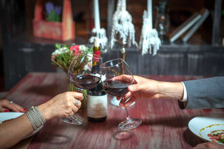 romantic couple with glasses of red wine on a date in a cozy Italian restaurant. Leisure, drinks, people and holidays concept - happy man and woman clinking glasses.の写真素材