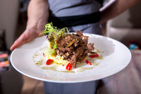 Waitress is carrying a plate with meat dishの写真素材