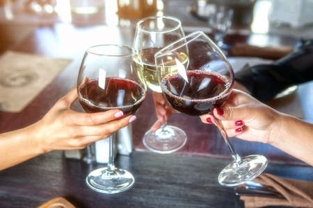 happy friends in a bar drinking red wine. Focus on glassesの写真素材