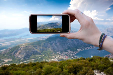 Woman tourist photographs on smartphone beautiful view of the mountain range in Montenegro. Travel concepts and technology. close upの写真素材