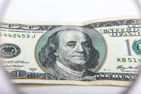 Dollar banknotes under magnifying glass. The concept of business: hundred-dollar bills are...