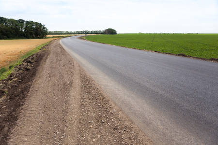 road in the countryside against a blue sky and white clouds surrounded by green grassの写真素材
