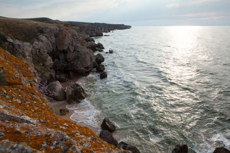 Wild beach with dark blue sea and cliffs with stones. Rocky coast on a sunny day. Coastline near the deep blue turquoise water. Beautiful sunny outdoor view of the wild and untouched seascape.の写真素材