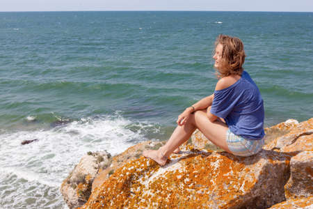 Young woman sitting on a rock with backpack and looking to the horizonの写真素材