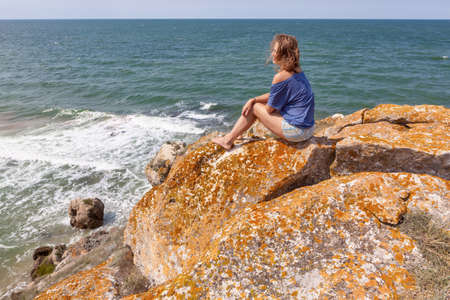 Young woman sitting on a rock with backpack and looking to the horizonの写真素材