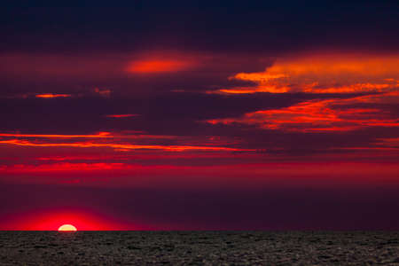 Beautiful red and orange sunset over the sea in a cloudy sky. The sun goes down over the sea. Two seagulls are flying against the sunset. Dramatic Sunset Skyの写真素材