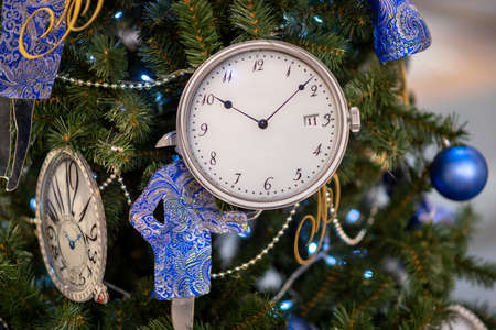 A Christmas tree toy in the form of the vintage clock with glittered hands. The New Year tree decorations with fairy lights and tinsel. Winter holidays background.の写真素材
