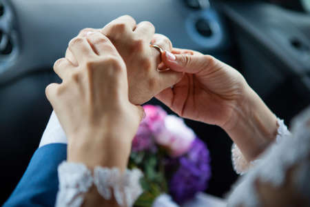 Young bride put a gold wedding ring on the grooms finger, close-up.