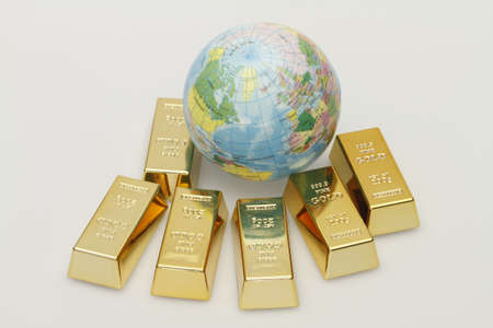 A small globe lies between six gold bars.の写真素材