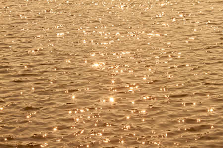 Sun rays reflected on a water surface in motion.の写真素材