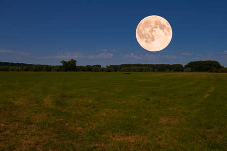 The bright full moon hovers over an idyllic landscape.の写真素材