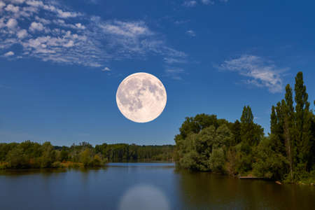 The bright full moon hovers over an idyllic landscape.の写真素材