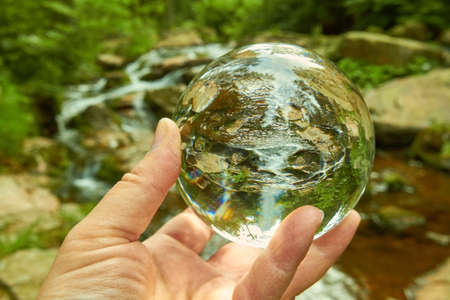 A hand holding a crystal ball on a creek.