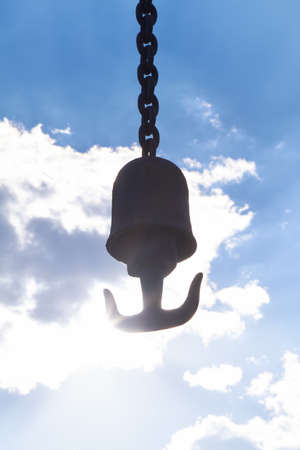 A hook hangs on an iron chain in bright sunshine.
