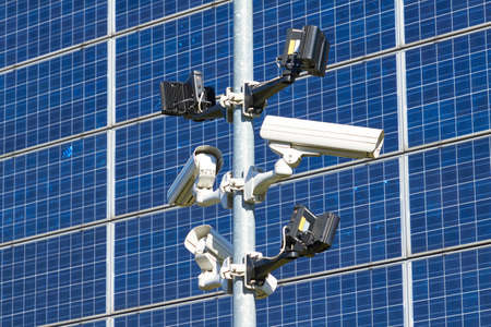 Surveillance cameras in front of a blue wall of solar cells in the sunshine.の写真素材