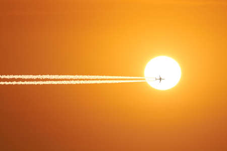 Sun and airplane with contrails on the orange sky.
