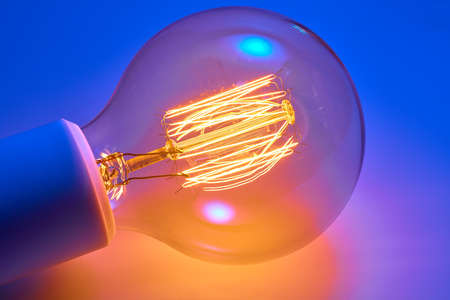 Old electric light bulb with orange luminous glow spiral.