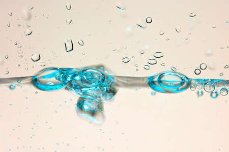 Close up of a blue water surface with water drops and air bubbles.