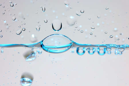 Close up of a blue water surface with water drops and air bubbles.