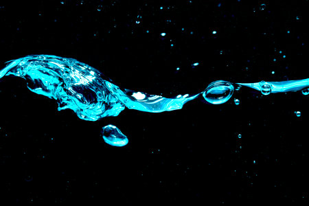 Close up of blue wave with water drops and air bubbles against a black background.