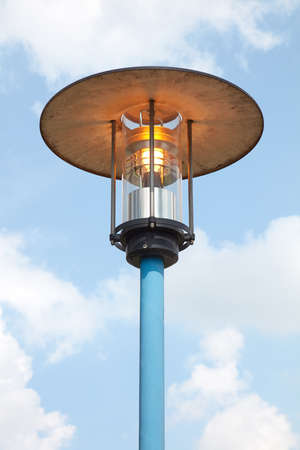 Shining street light on the side of the road during the day.