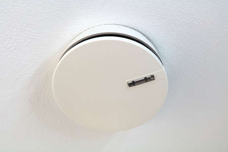 An electronic smoke detector hangs under a white ceiling.