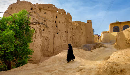 woman in a hijab passes by the destroyed fortress in the villageのeditorial素材
