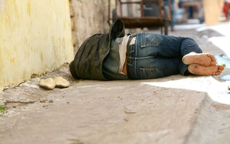 tramp lies on the road, footwear is put by a row, has a rest lying on the sidewalkのeditorial素材