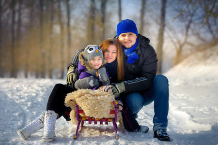 the happy close-knit family poses on the sledge in the winter woodの写真素材