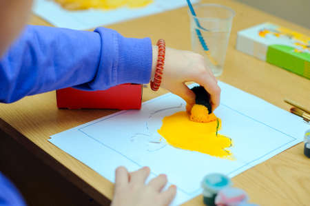 ?hild, Boy of school age, does hand-made articles on a school table, accurately decorates with a sponge a contour, application on the sheet of paperの写真素材